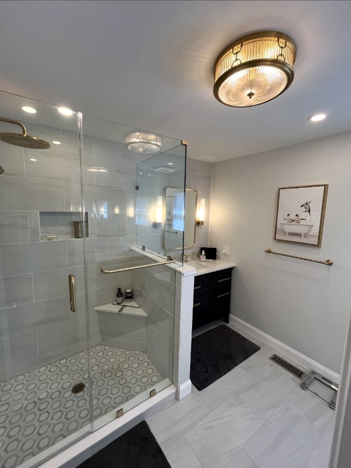 Bathroom with a frameless glass shower, brass hardware, built-in bench, patterned floor tile, and dark vanity cabinetry.