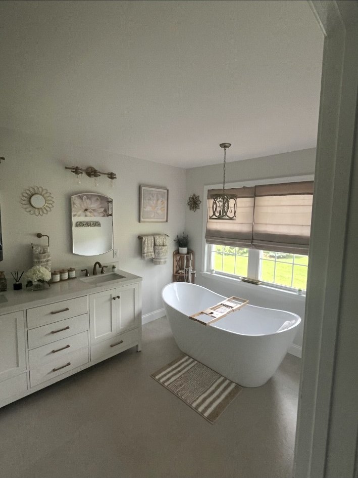 Bathroom with a freestanding soaking tub, detailed vanity cabinetry, mirror, sconce, window shade, and decorative pendant light.