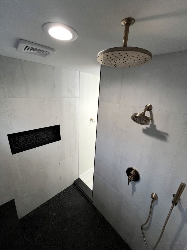 Custom walk-in shower with a ceiling rain head, wall shower, handheld fixture, niche, bench, and dark pebble floor.