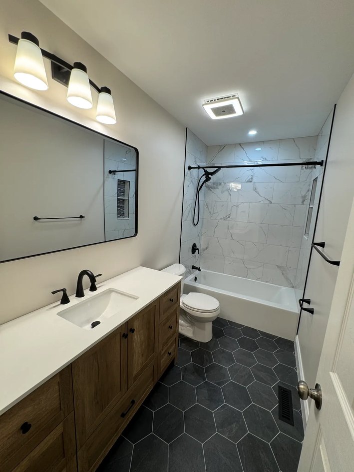 Oak vanity bathroom with dark hex floor and stone-look tub surround.