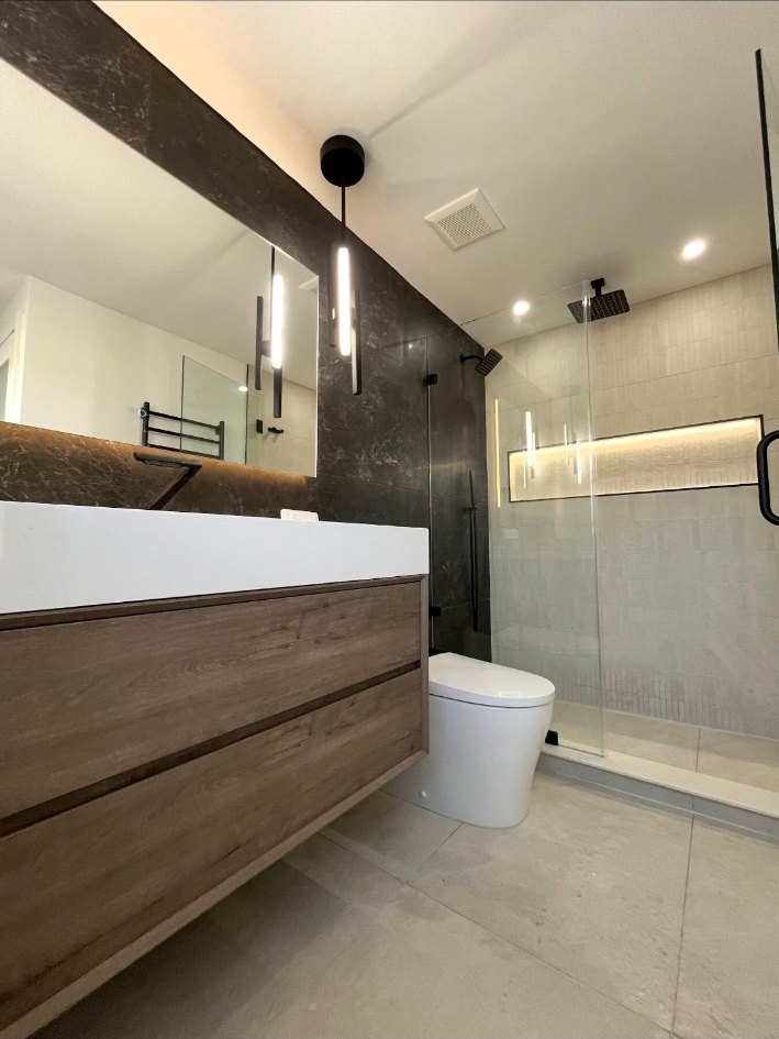 Low-angle view of a floating wood vanity, integrated sink, vertical pendant light, and frameless shower in Richboro.