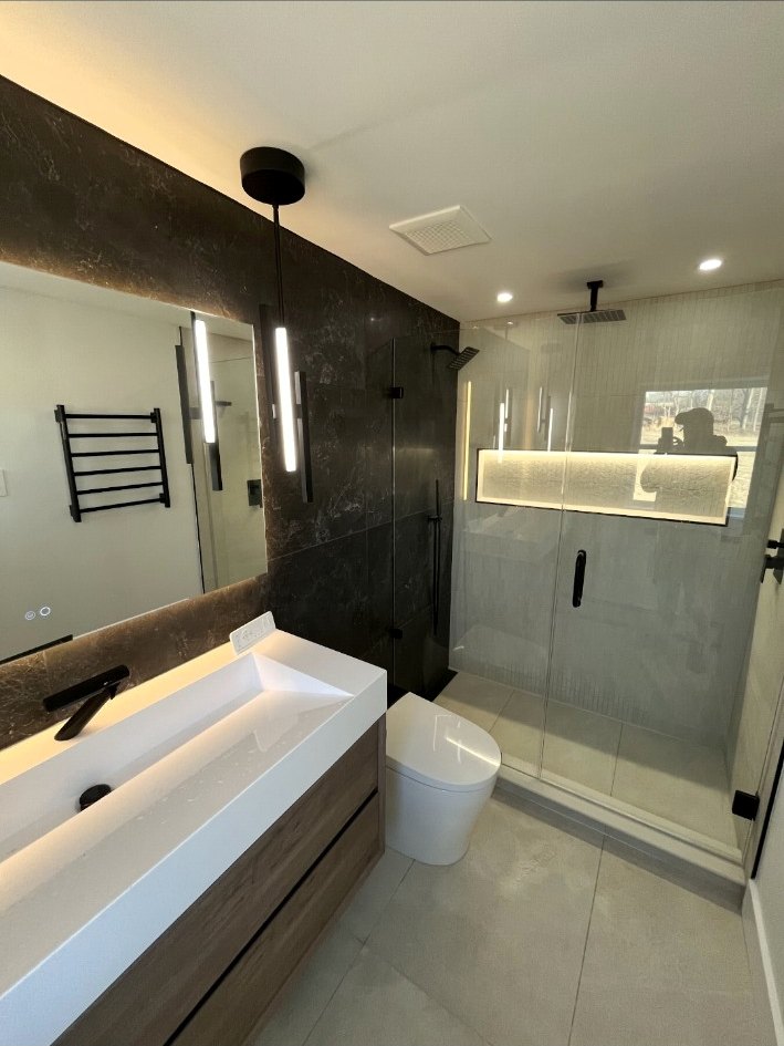 Modern Richboro bathroom with a floating wood vanity, dark stone accent wall, frameless shower, and illuminated niche.