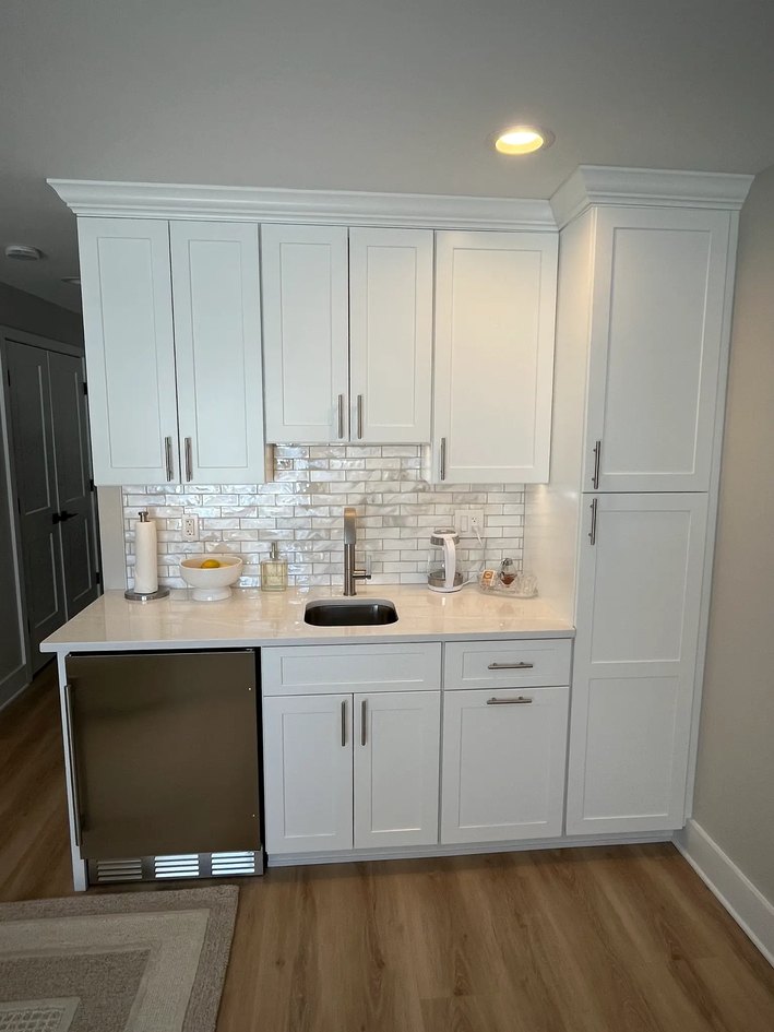 White Shaker beverage center with sink, undercounter refrigerator, and tile backsplash.