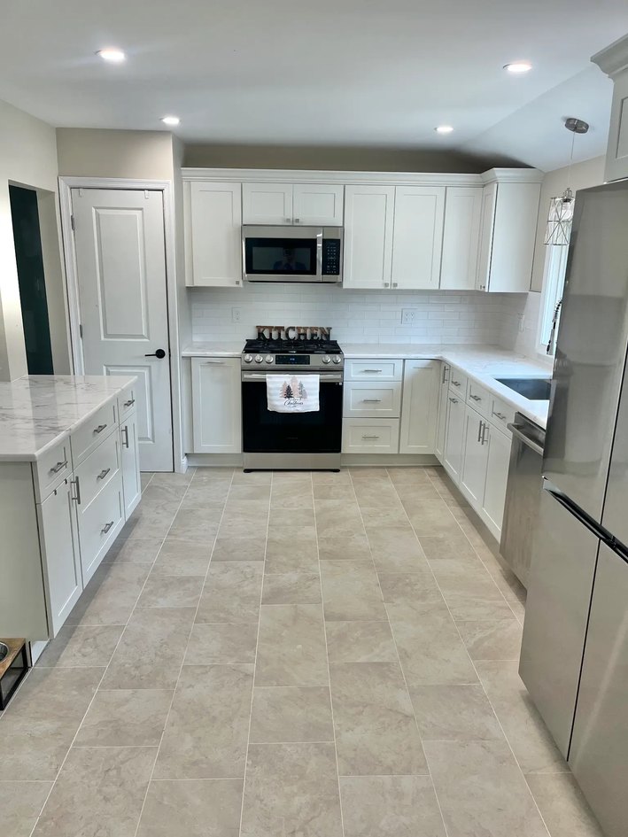 White Shaker kitchen with stone counters, stainless appliances, and tiled floor.